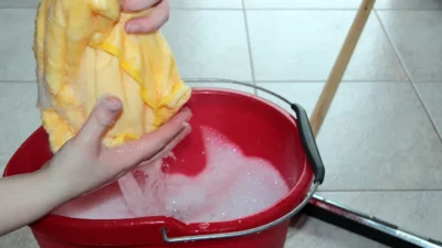 A person cleaning different floor types: ceramic tile, vinyl plank, and wood-look laminate with appropriate tools.