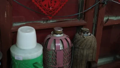 A person holding a spray bottle and cloth, confused by unlabeled cleaning supplies on a cluttered shelf.