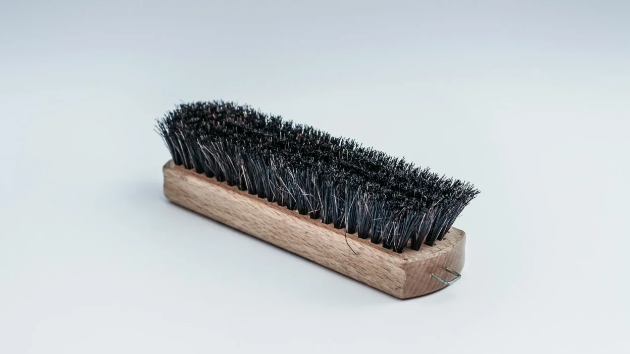 Close-up comparison of a scrub brush and sponge cleaning bathroom tile grout