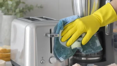 Person wiping the exterior of a stainless steel blender with a microfiber cloth for cleaning small appliances.