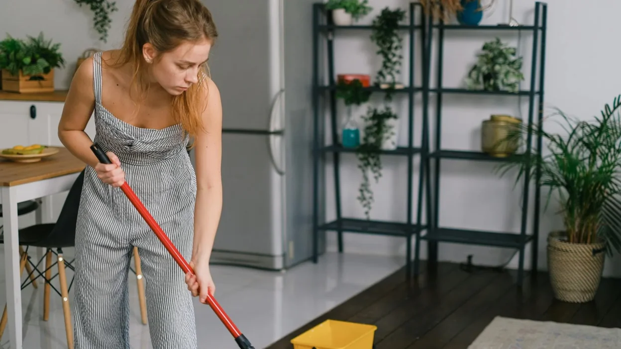 Person using too much water while mopping a hardwood floor, causing potential water damage.
