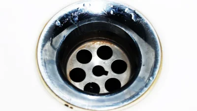 Woman cleaning a kitchen sink with baking soda and vinegar to eliminate foul odors